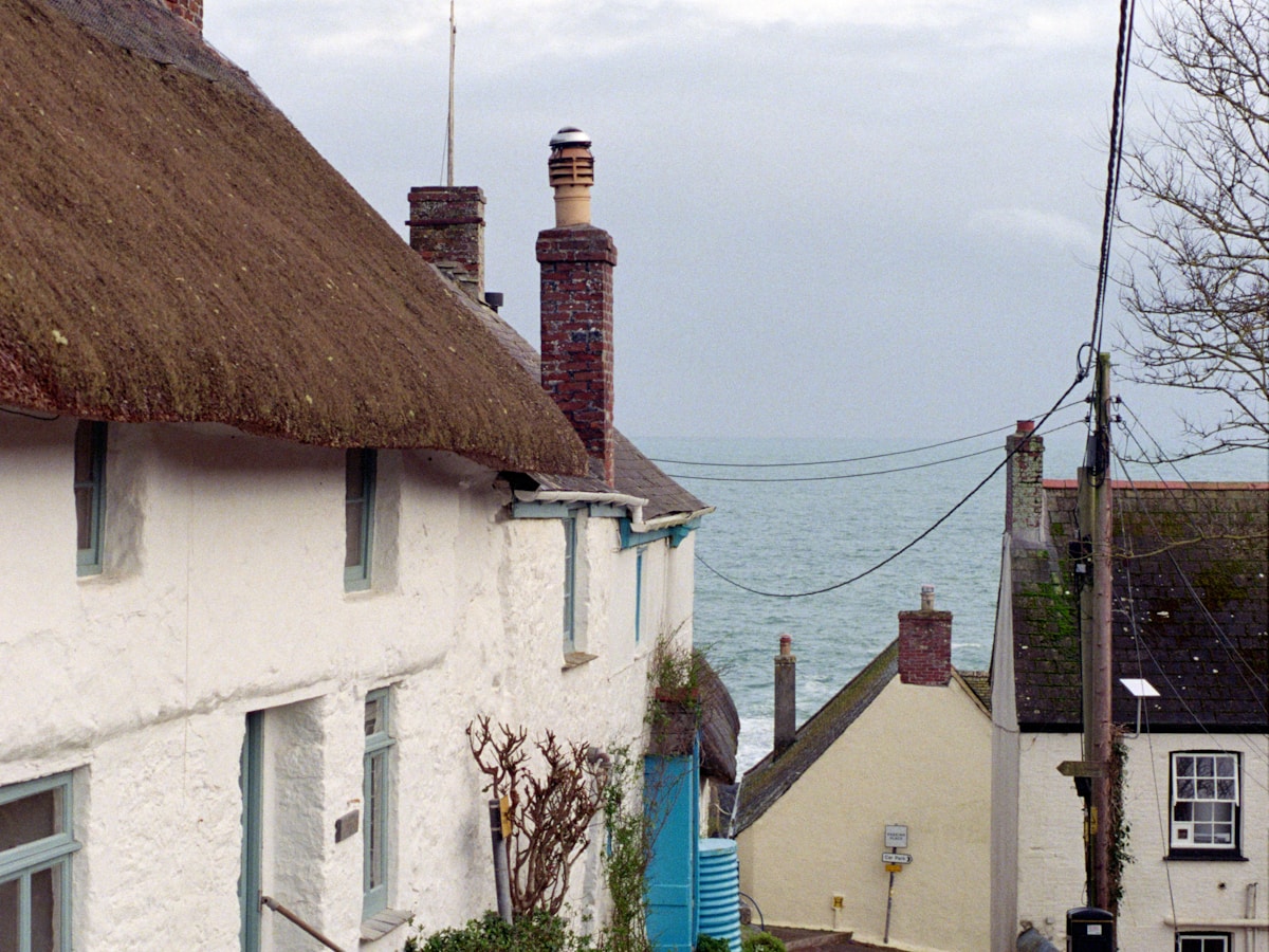 Thatched cottages on a Cornish lane with the sea beyond