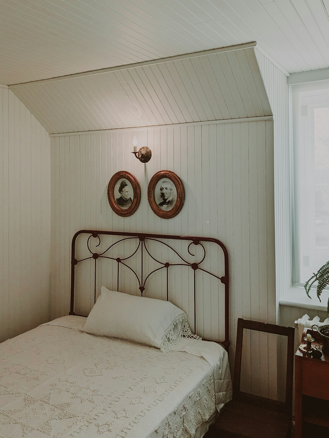 The Lookout room: tongue-and-groove panelled walls under the eaves, an iron bedframe and Victorian portraits